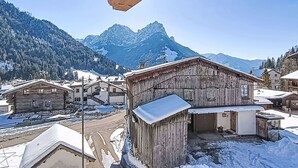 Een houten gebouw met een met sneeuw bedekte dak, omgeven door andere gebouwen en een bergachtige achtergrond.