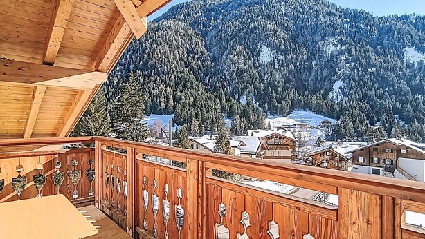 Een houten balkon met uitzicht op een met sneeuw bedekte berg en een dorp daaronder.
