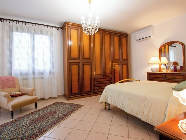 Una camera da letto con un letto, una sedia, un armadio, un lampadario e una cassettiera con uno specchio.