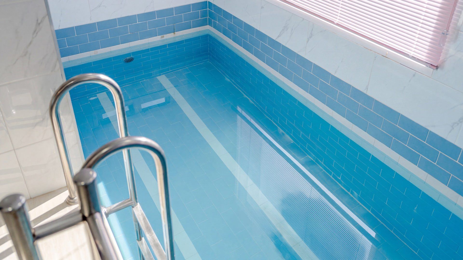 En swimmingpool med en metalstige og blå fliser.