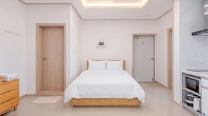 Une chambre d’hôtel comprenant un lit, une commode en bois, une kitchenette et une salle de bain.