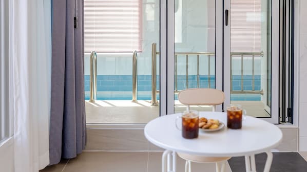 Un balcon avec une porte vitrée, une chaise blanche et une table avec des boissons et des en-cas.