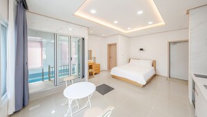 Une chambre d’hôtel moderne dotée d’un grand lit, d’un bureau avec une chaise, d’une petite table et d’un balcon avec une porte vitrée.