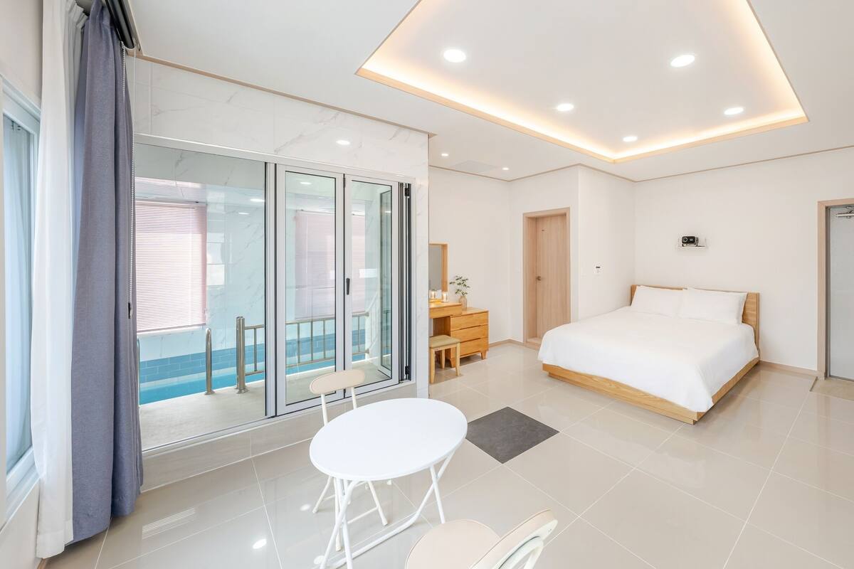 Ein modernes Hotelzimmer mit einem großen Bett, einem Schreibtisch mit Stuhl, einem kleinen Tisch und einem Balkon mit Glastür.