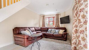 Ein Wohnzimmer mit einem braunen Ledersofa, einem kleinen runden Tisch und einem Fenster mit Vorhängen.