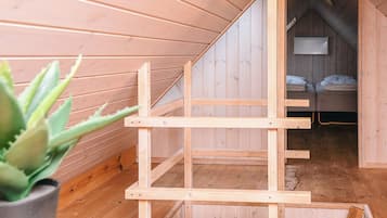 Un interior de madera con techo inclinado, una cama con almohadas y una planta en maceta.