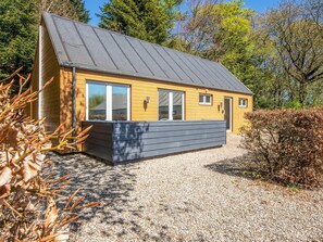 A small, single-story building with a sloped roof, large windows, and a gravel driveway.