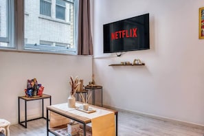 A modern living room with a flat-screen TV mounted on the wall, a wooden coffee table, a small side table with snacks, and a window with curtains. - Premium Central Liverpool Apartment | Sleeps 4 (Liverpool)