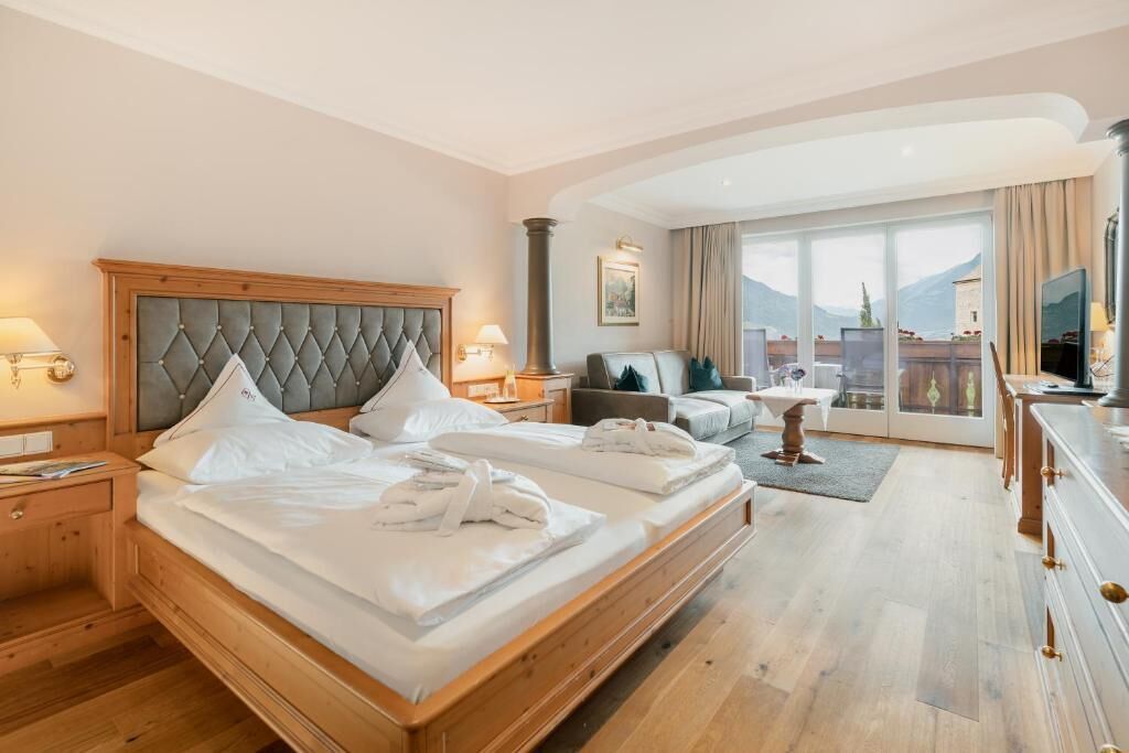 Una habitación de hotel con una cama grande, un sofá, un televisor y vistas a las montañas.