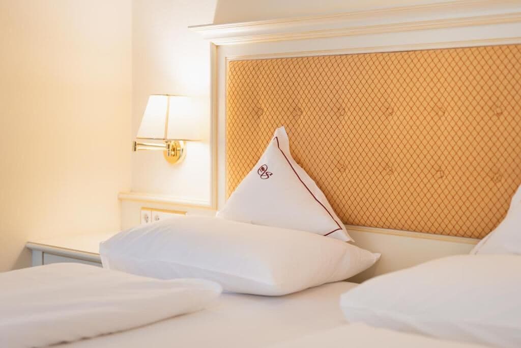 Una habitación de hotel con una cama, almohadas, un cabecero y una lámpara fijada a la pared.