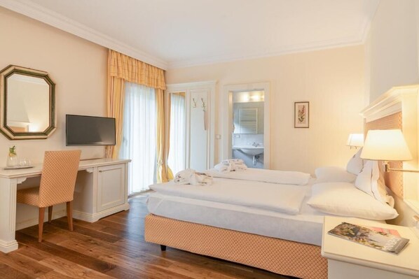 Quarto de hotel com cama, escrivaninha, televisão e banheiro visível por uma porta aberta.
