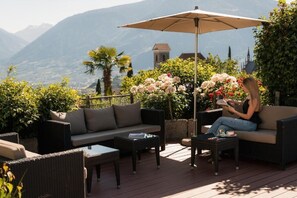 Uma área externa com mobiliário de vime, uma mesa e um guarda-sol.