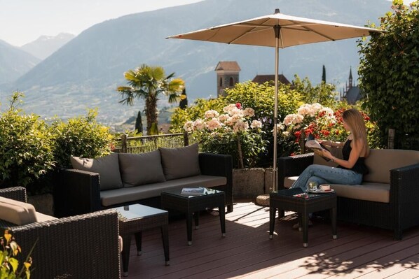 An outdoor seating area with wicker furniture, a table, and an umbrella. - Hotel Starkenberg (Schenna)