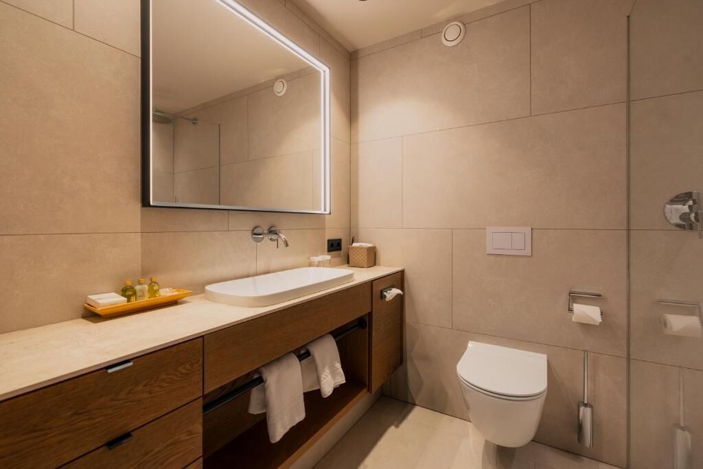Uma casa de banho moderna com um espelho grande, uma pia, uma sanita e um porta-toalhas.