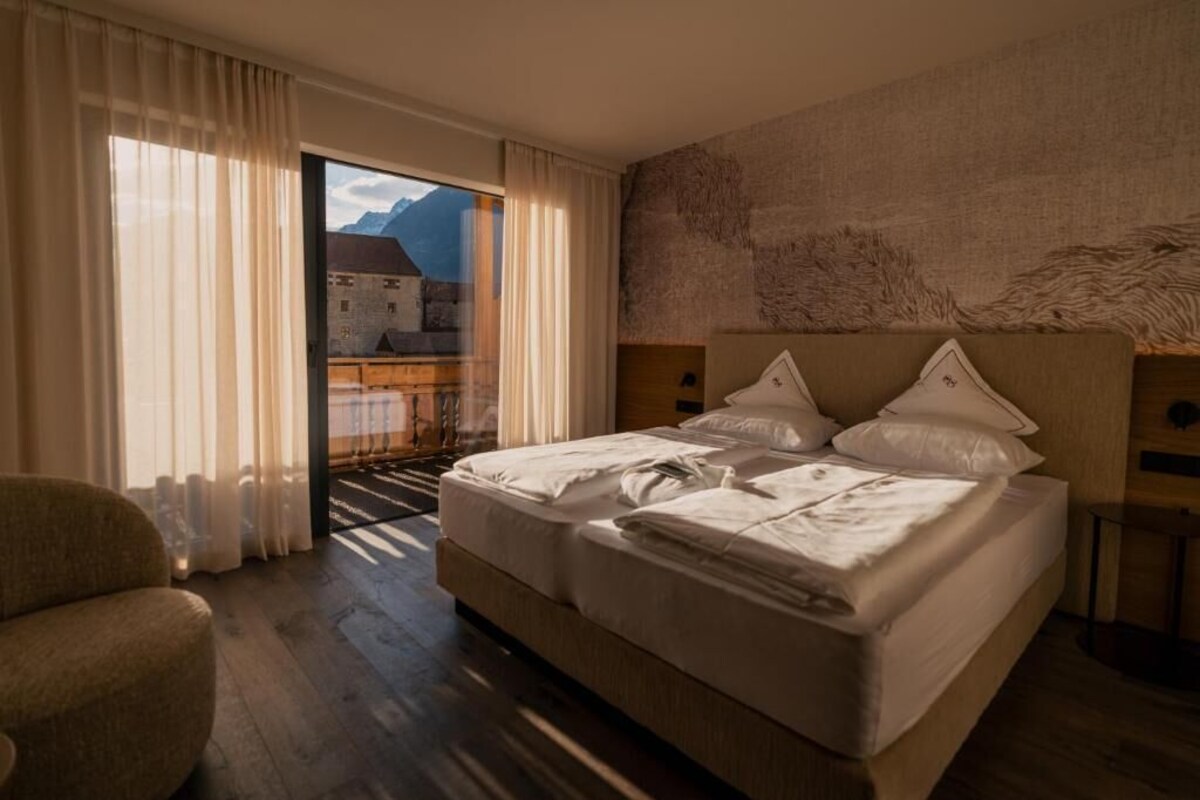 A hotel room with a large bed, a chair, and a view of a mountain through a window.