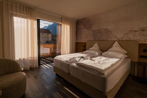 A hotel room with a large bed, a chair, and a view of a mountain through a window. - Hotel Starkenberg (Schenna)