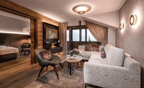Et moderne hotelværelse med seng, sofa, stol, et lille bord med en vase og et stort vindue med gardiner.