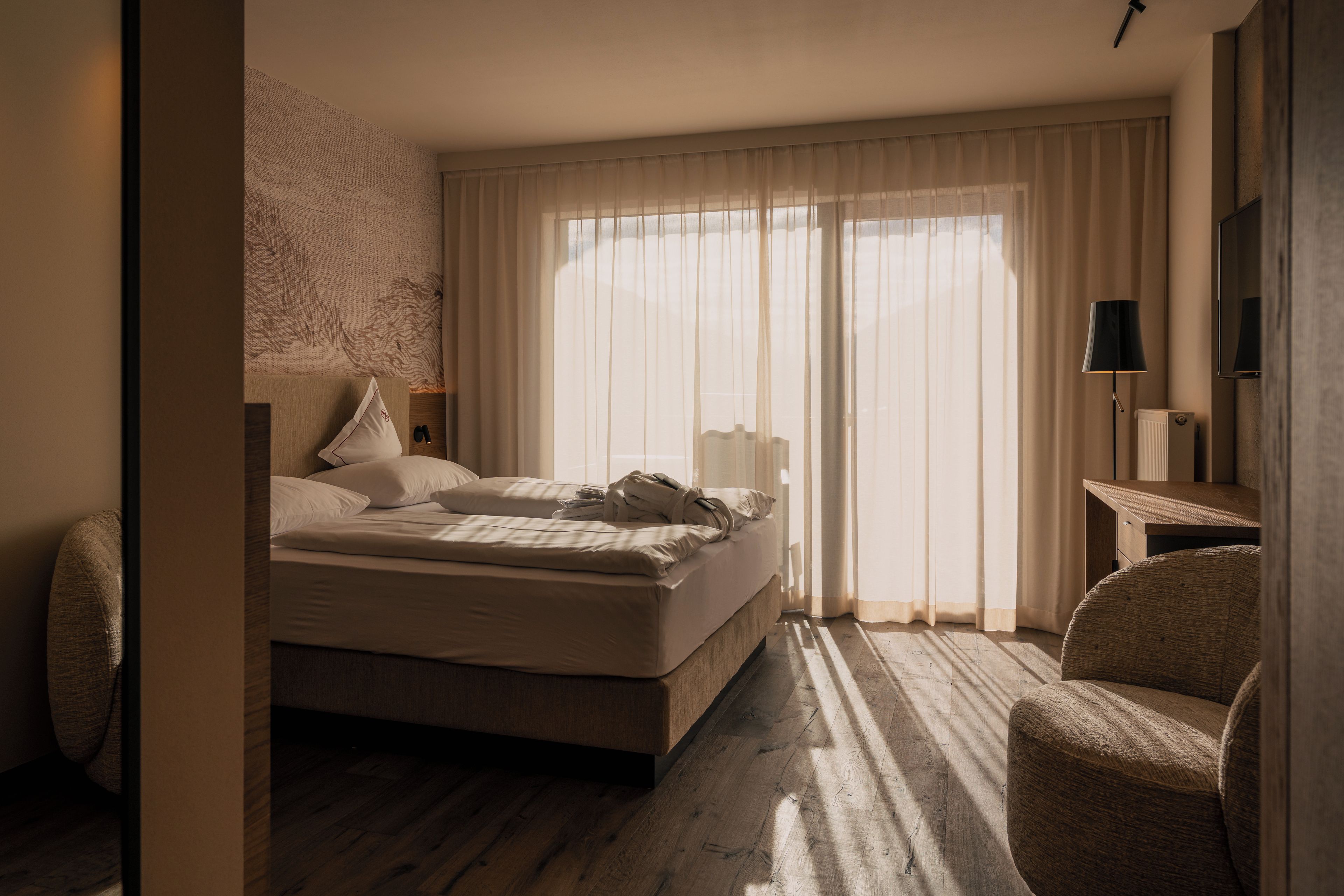 Een hotelkamer met een bed, een stoel, een bureau en een groot raam met gordijnen.