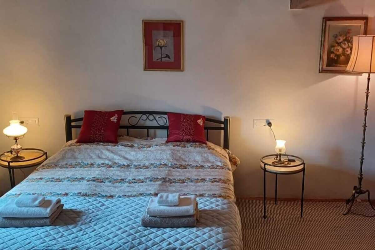 En snyggt bäddad säng med ett täcke, två kuddar, två sänglampor och två hopvikta handdukar.
