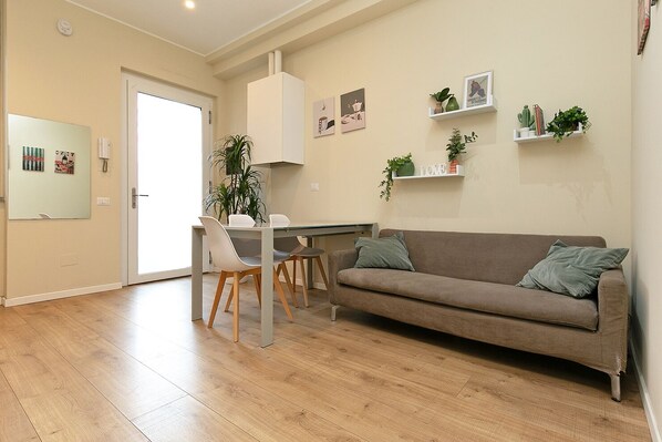A modern living room with a brown sofa, a dining table with chairs, and a kitchen area. - Suite Roma 53 - Two-room apartment in downtown Saronno, within walking distance of the train station (Saronno)