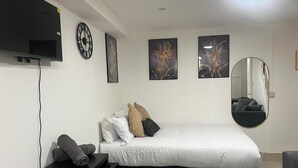 Un dormitorio moderno con cama, escritorio, televisor de pantalla plana y obras de arte en las paredes.