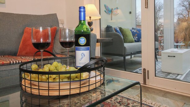 A living room with a glass table holding a bottle of wine, glasses, and a bowl of grapes. - Riverside Cottage (Shrewsbury)