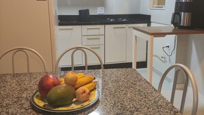 Uma cozinha com bancada de granito, uma fruteira com maçãs e bananas, uma geladeira e uma cafeteira.