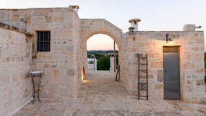 A stone courtyard with an archway, a small table, and a door with a ladder. - Authentic Trulli Stay with Private Pool and Panoramic Views | Itria Valley (Martina Franca)