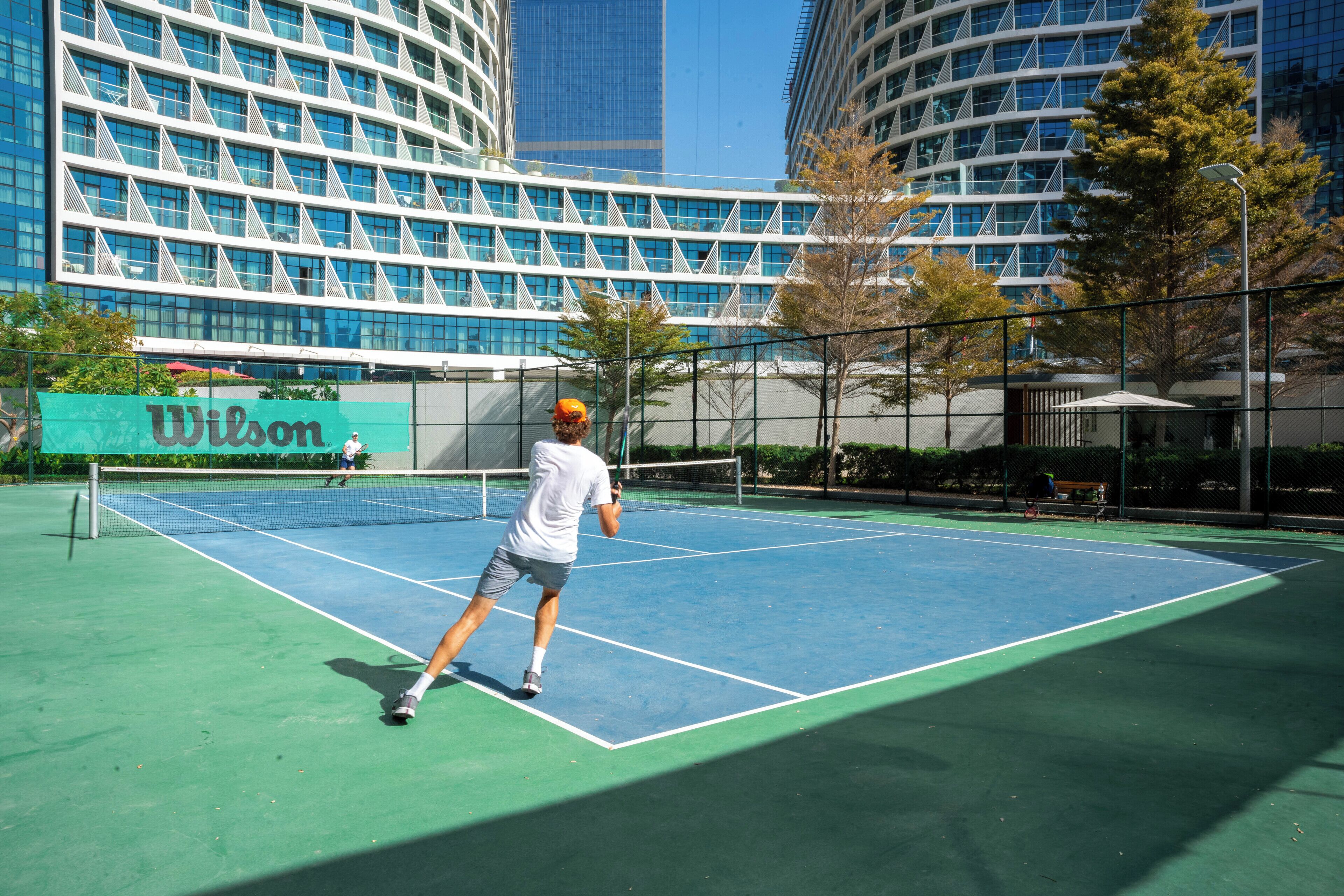 Un court de tennis avec un filet, entouré d’arbres et de bâtiments.