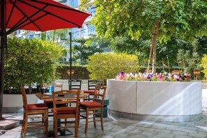 An outdoor seating area with wooden tables and chairs, a red umbrella, and a planter with colorful flowers. - Luxury Studio with  Private Beach (Dubai)
