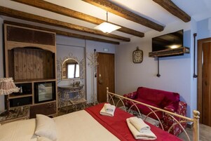 A room with a bed, a red chair, a wooden cabinet, a mirror, and a television mounted on the wall.