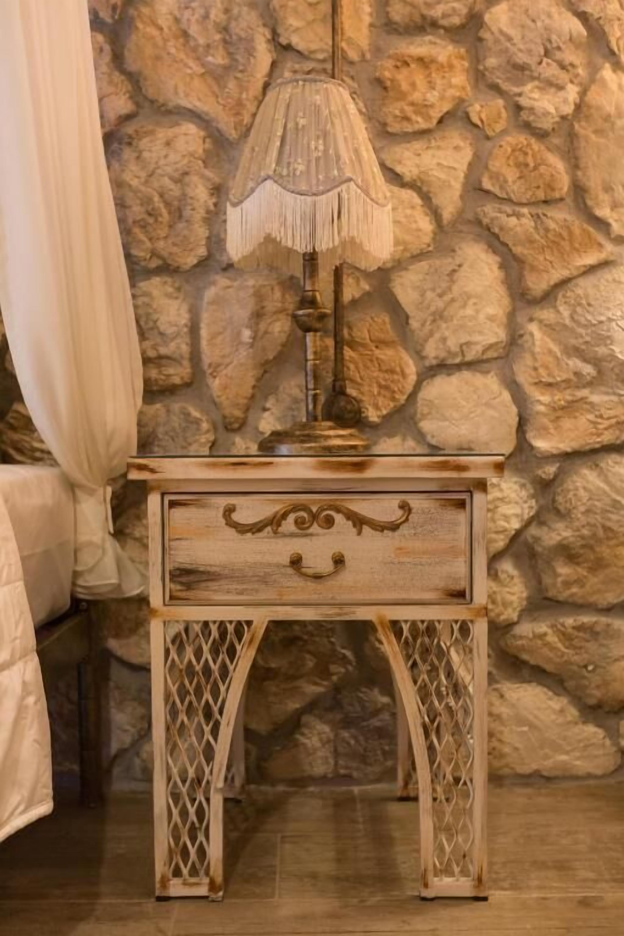 Ein Nachttisch aus Holz mit einer dekorativen Lampe vor einer Steinwand.