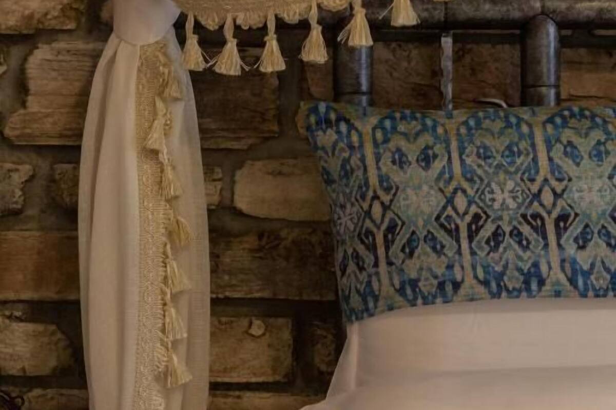 Ein Bett mit einem weiß-blauen Kopfschild, einem weißen Baldachin mit Fransen und einer Wand aus Stein im Hintergrund.