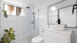 Un baño moderno con azulejos blancos, un inodoro, un lavabo con espejo y una zona de ducha.