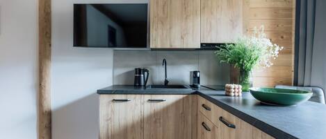 A modern kitchen with wooden cabinets, a black countertop, and a flat-screen TV mounted above the sink.