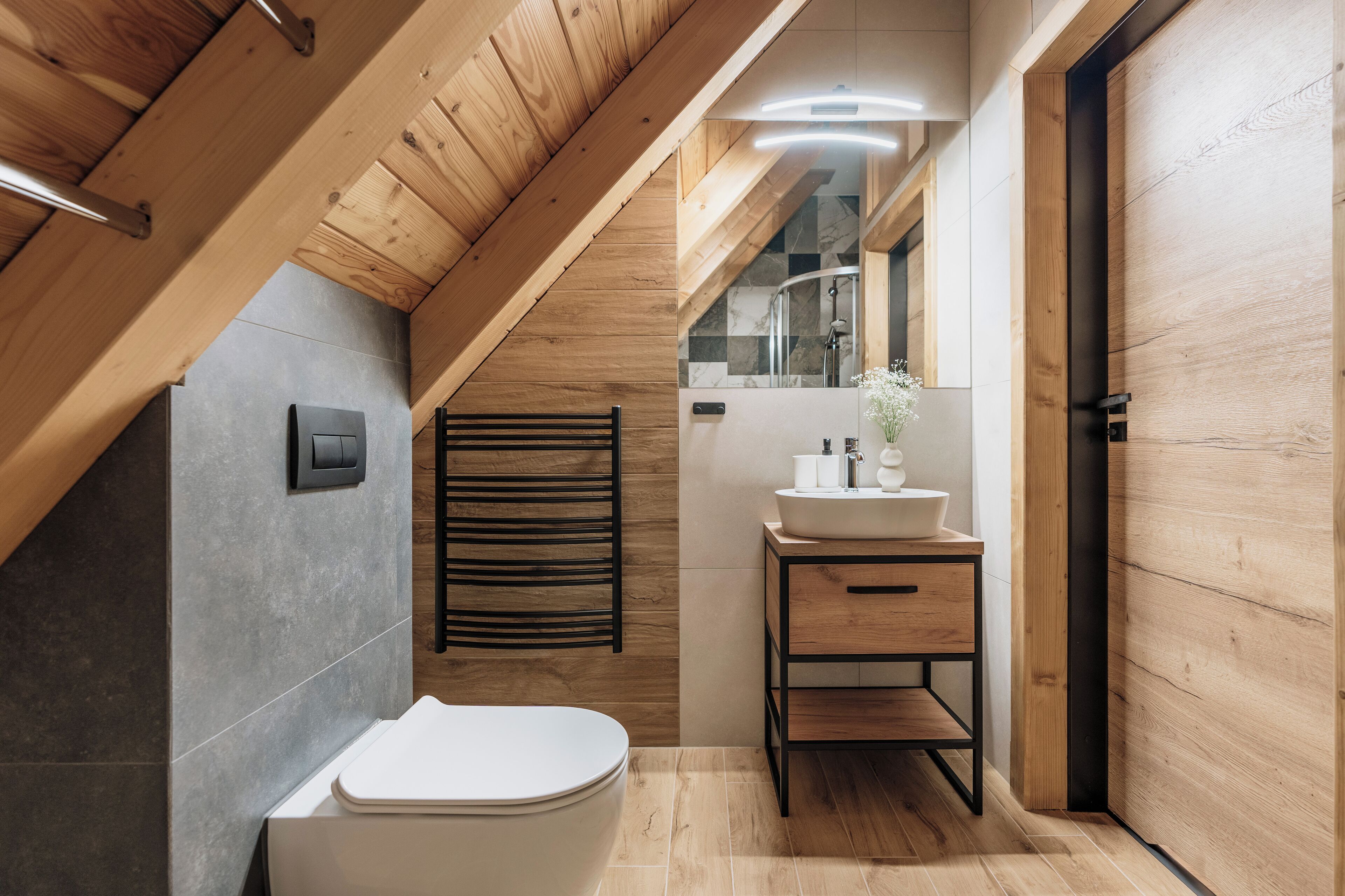 Et moderne badeværelse med træloft, et hvidt toilet, en vask med spejl og en håndklædestang.