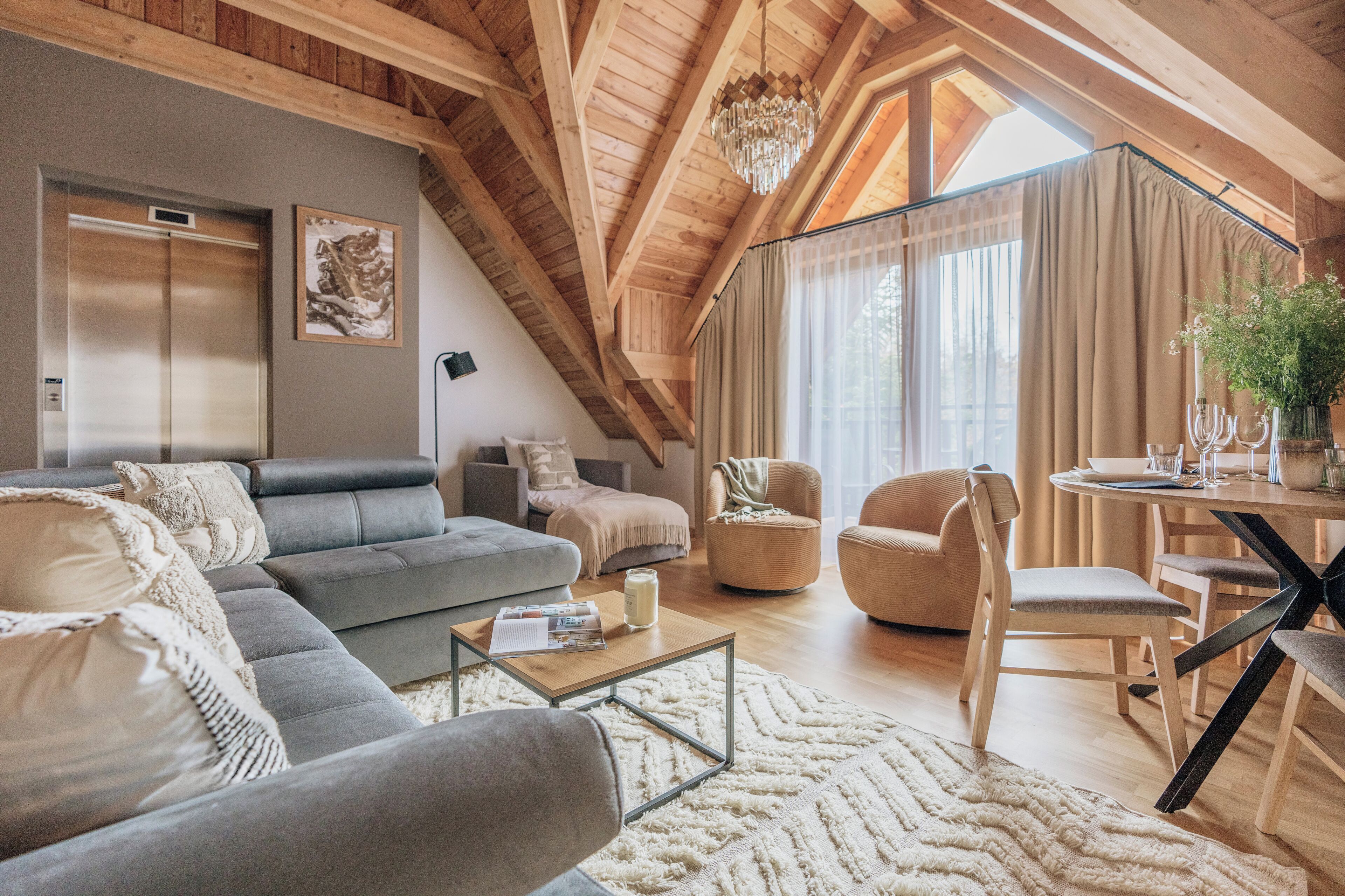 Amplio espacio tipo loft con techo alto, vigas de madera, un gran ventanal con cortinas, una mesa de comedor con sillas y un moderno conjunto de sofás.