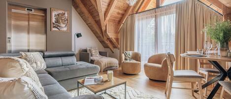 Amplio espacio tipo loft con techo alto, vigas de madera, un gran ventanal con cortinas, una mesa de comedor con sillas y un moderno conjunto de sofás.