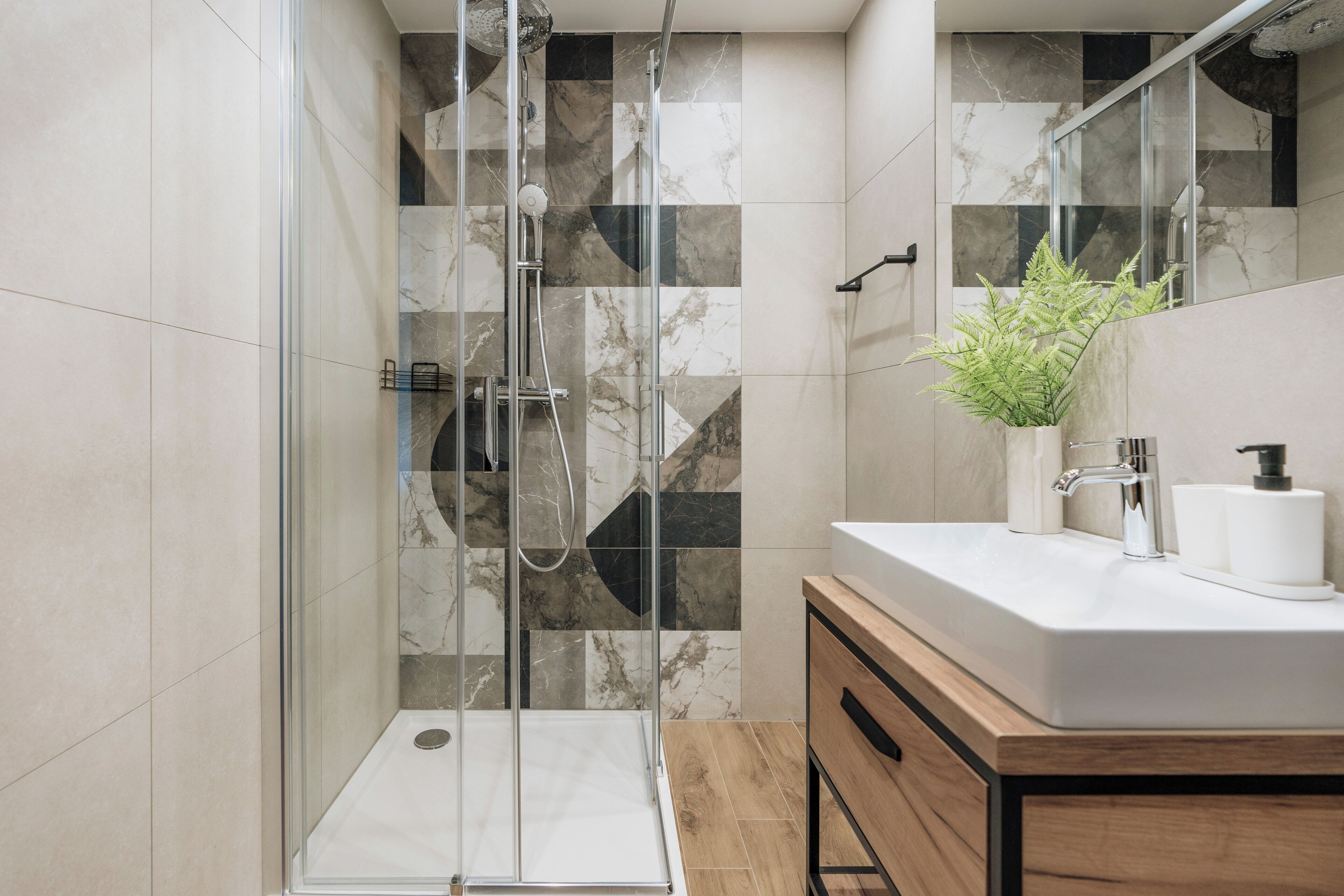 Een moderne badkamer met een douche in een glazen cabine, een houten wastafelmeubel en een wand betegeld met marmer.