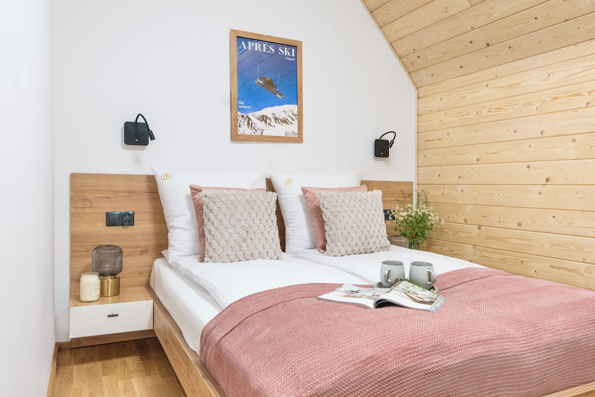 A neatly made bed with a magazine, two mugs, and a decorative item on the nightstand.
