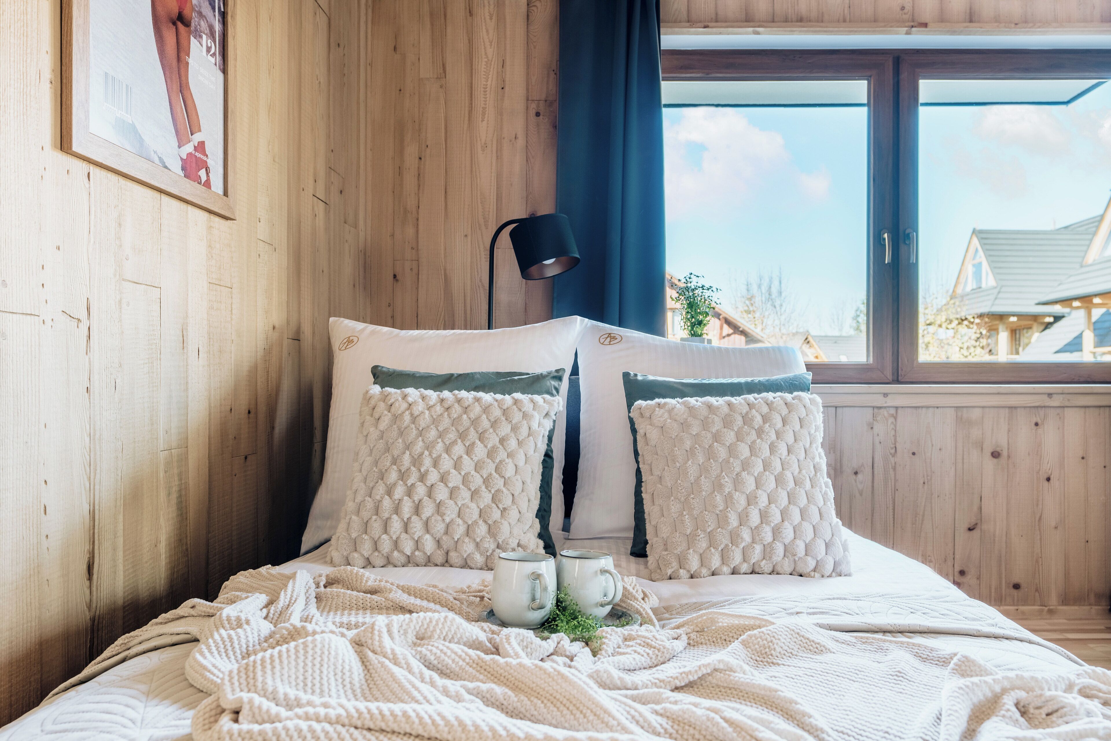 Un dormitorio acogedor con pared de madera, un ventanal grande y una cama con almohadones blancos y azul marino.