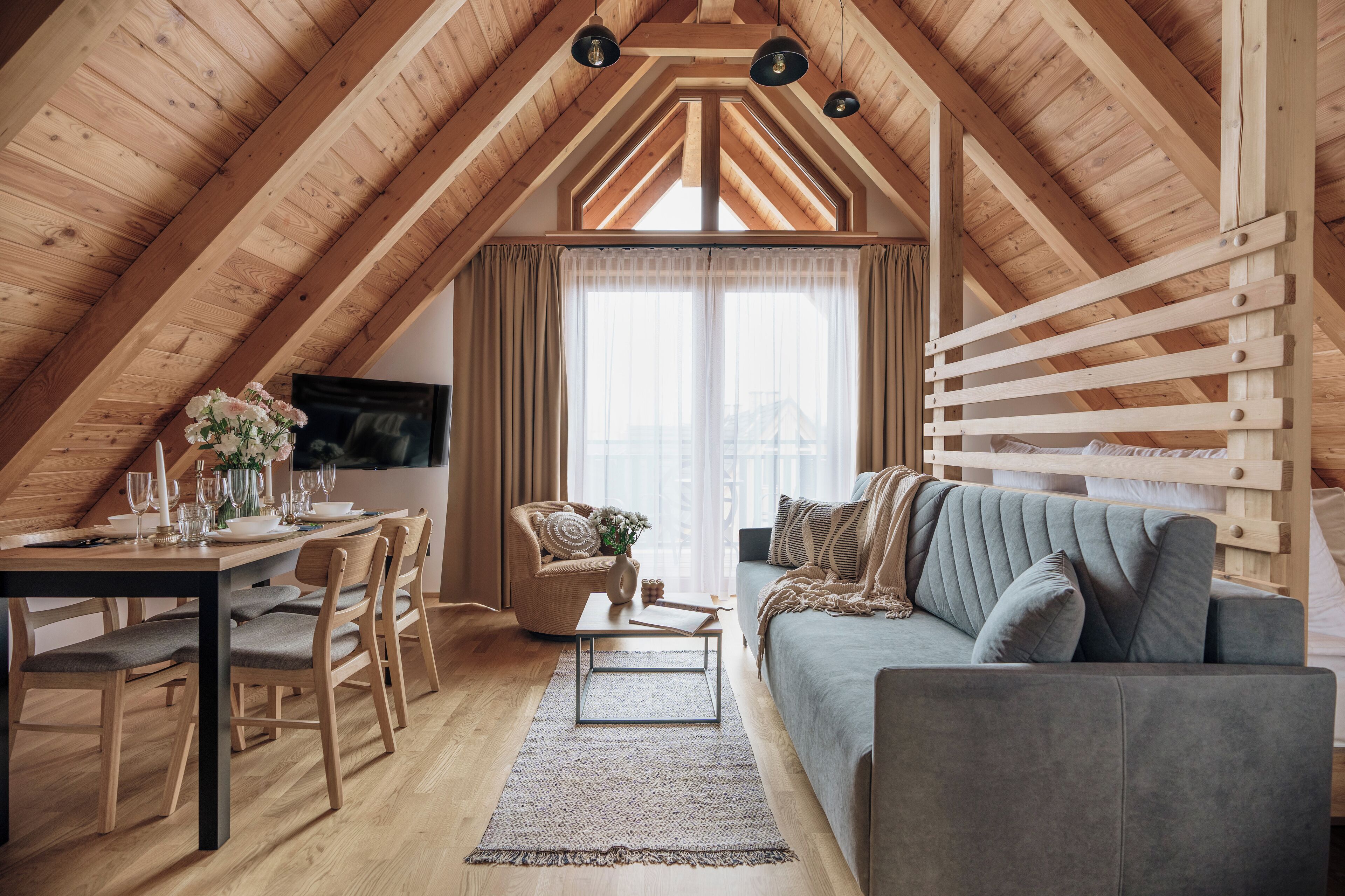 A cozy attic room with a dining area, a sofa, and a TV mounted on the wall.