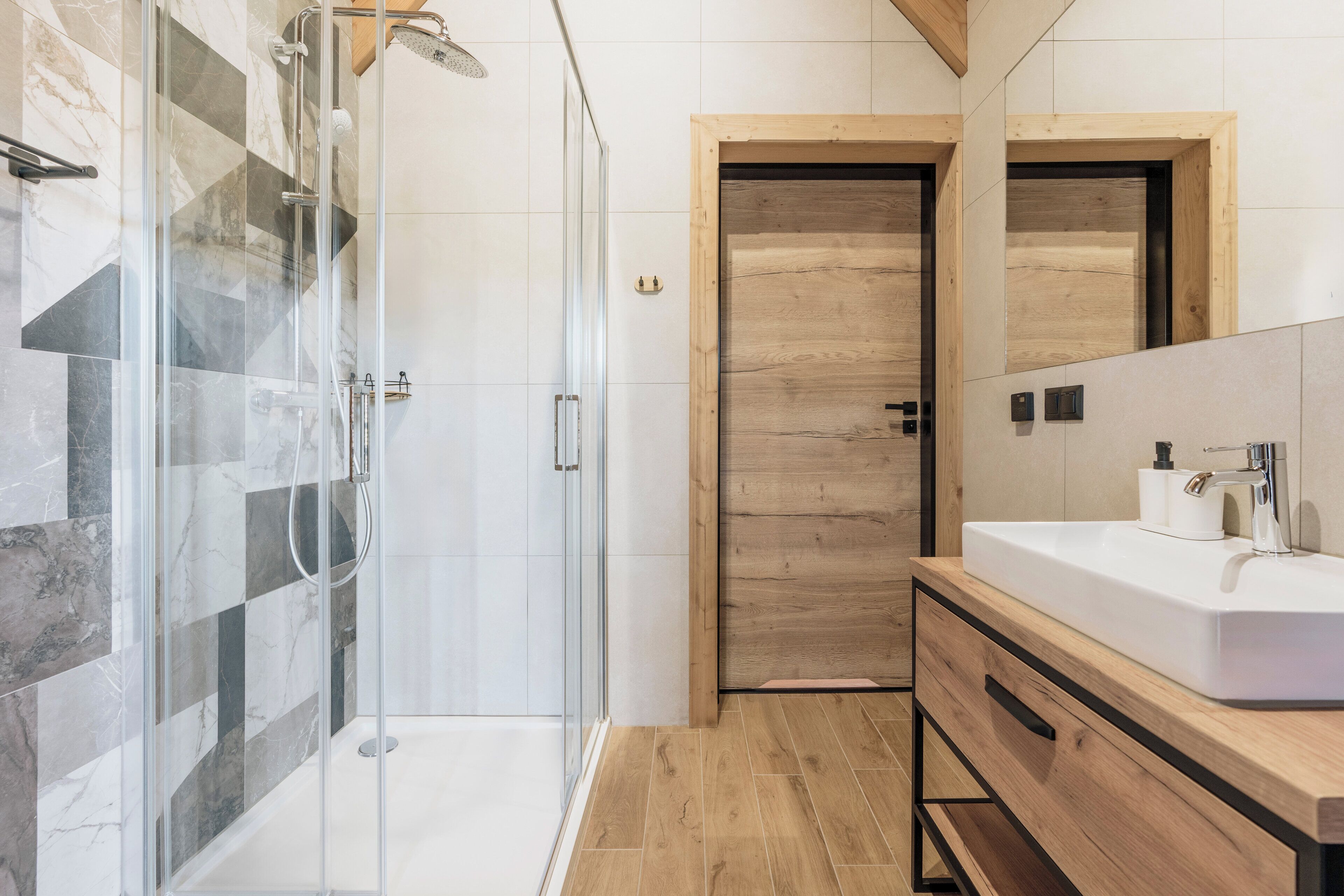 Un baño moderno con cabina de ducha de vidrio, puerta de madera y un lavabo grande con tocador de madera.