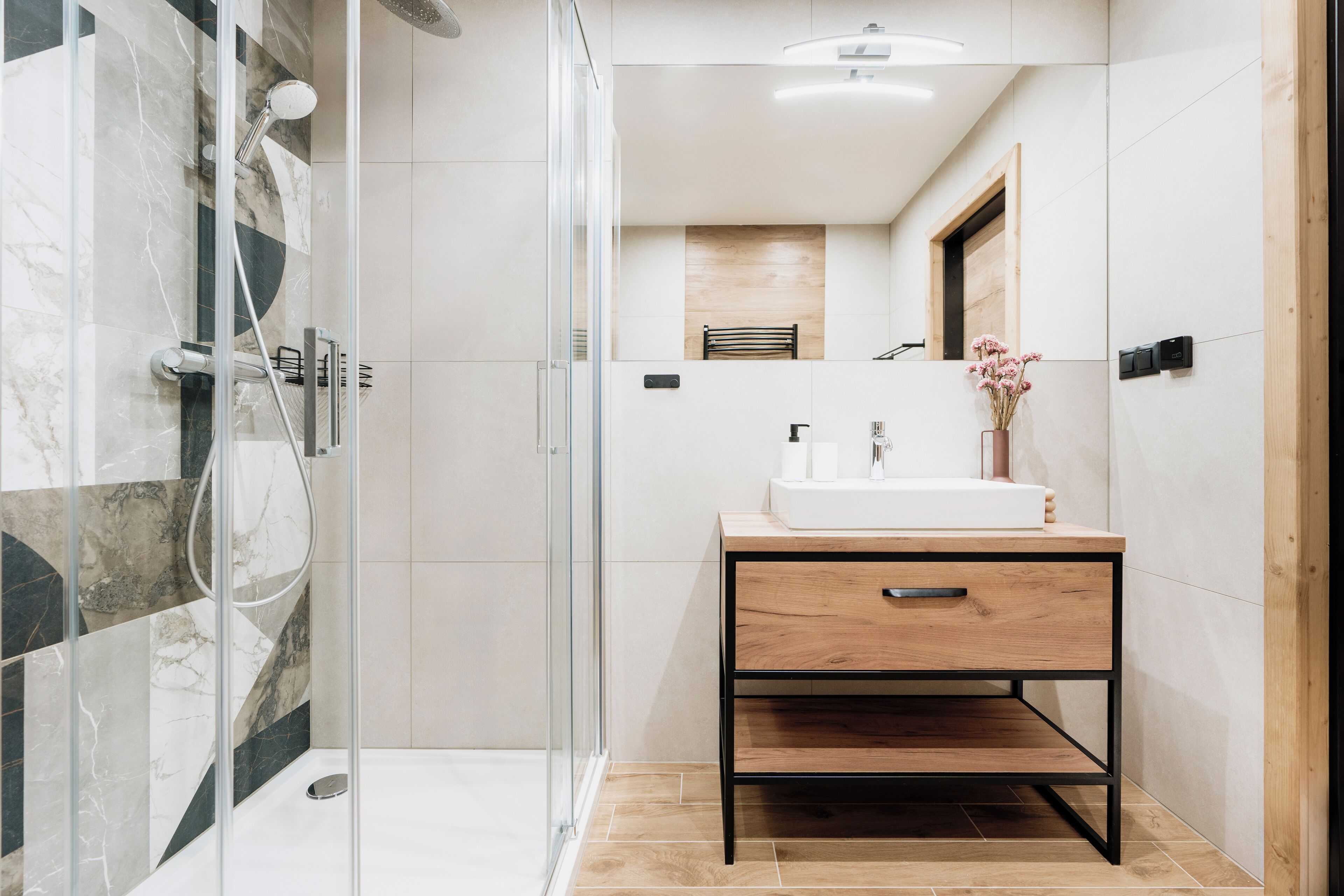 A modern bathroom with a glass-enclosed shower, a wooden vanity with a sink, and a mirror above it.