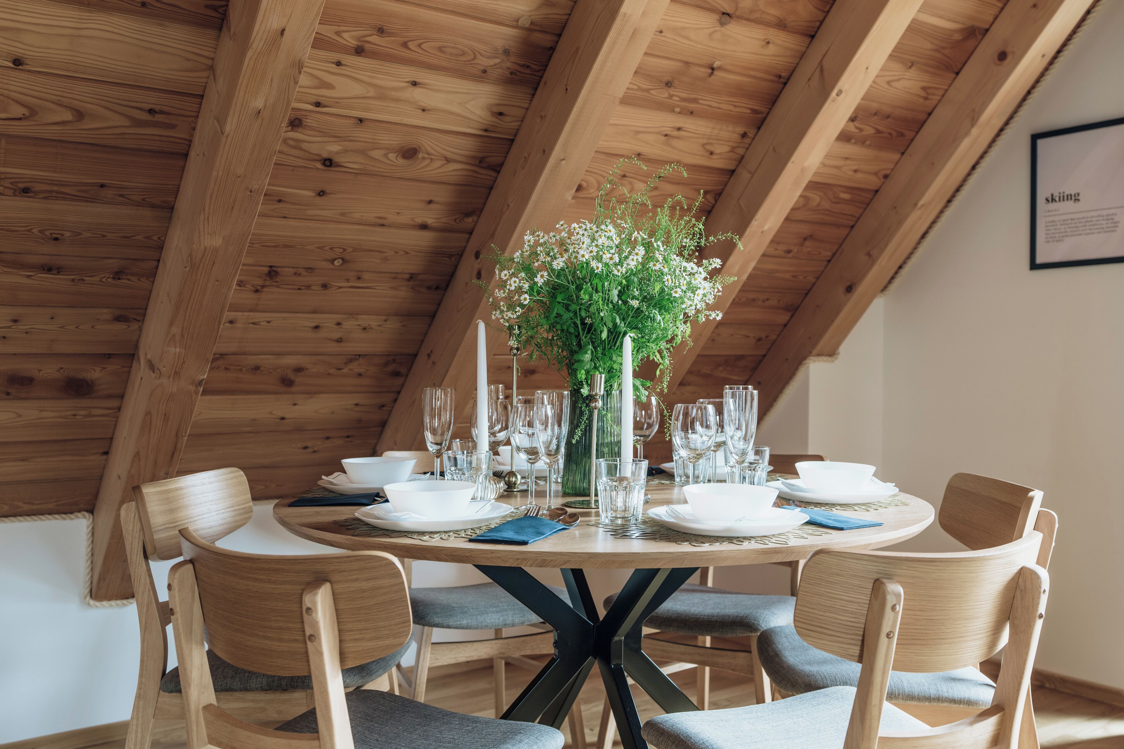 A wooden dining table set with white plates, glasses, and a vase of flowers.