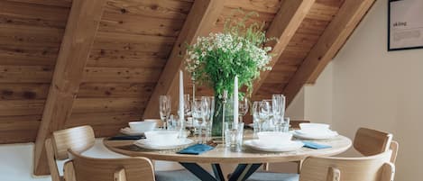 A wooden dining table set with white plates, glasses, and a vase of flowers.