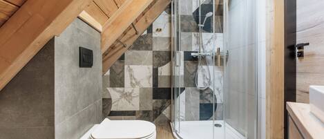 A modern bathroom with a glass shower enclosure, a white toilet, and a tiled floor.