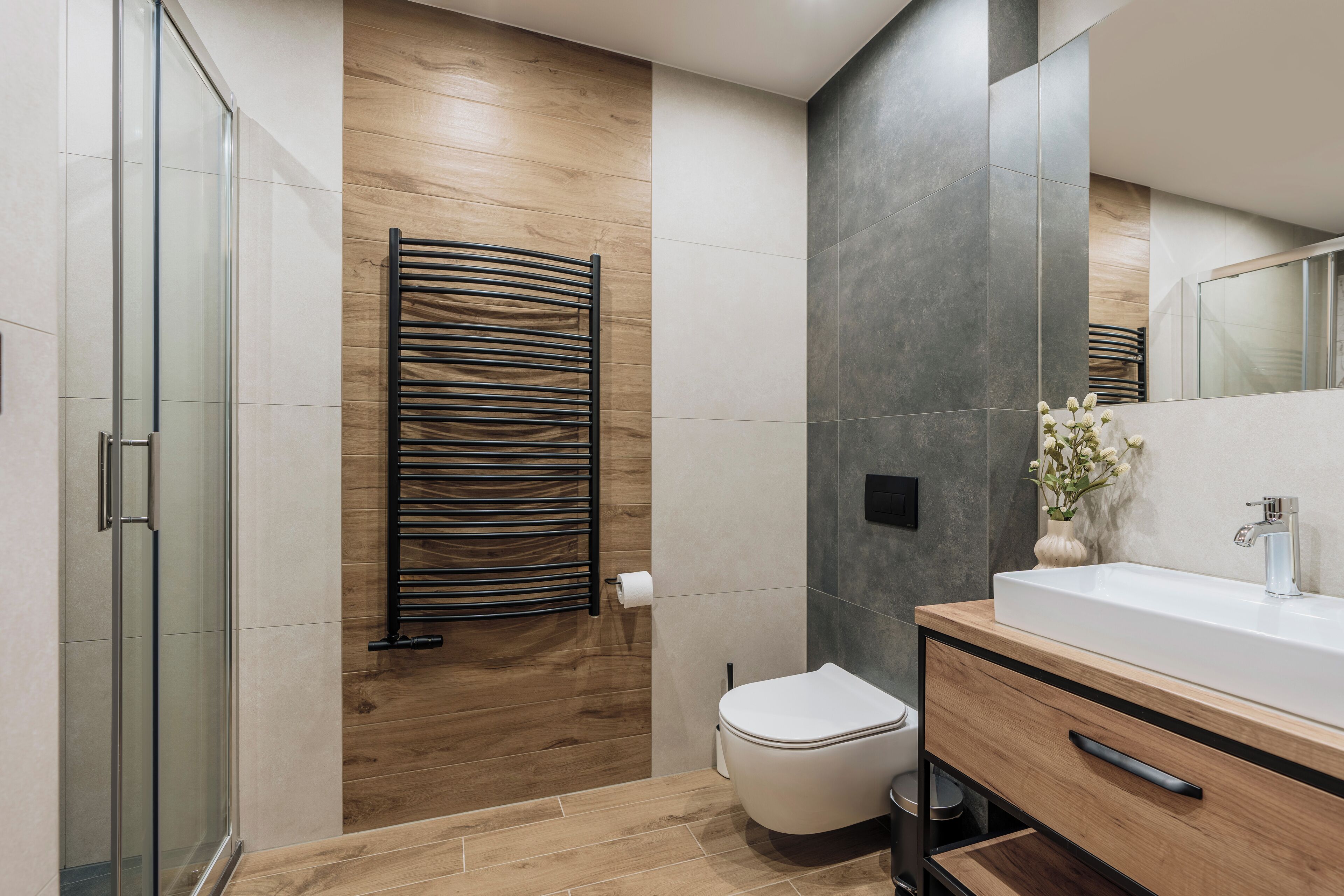 Un baño moderno con cabina de ducha de vidrio, pared de madera, inodoro blanco y tocador con espejo.