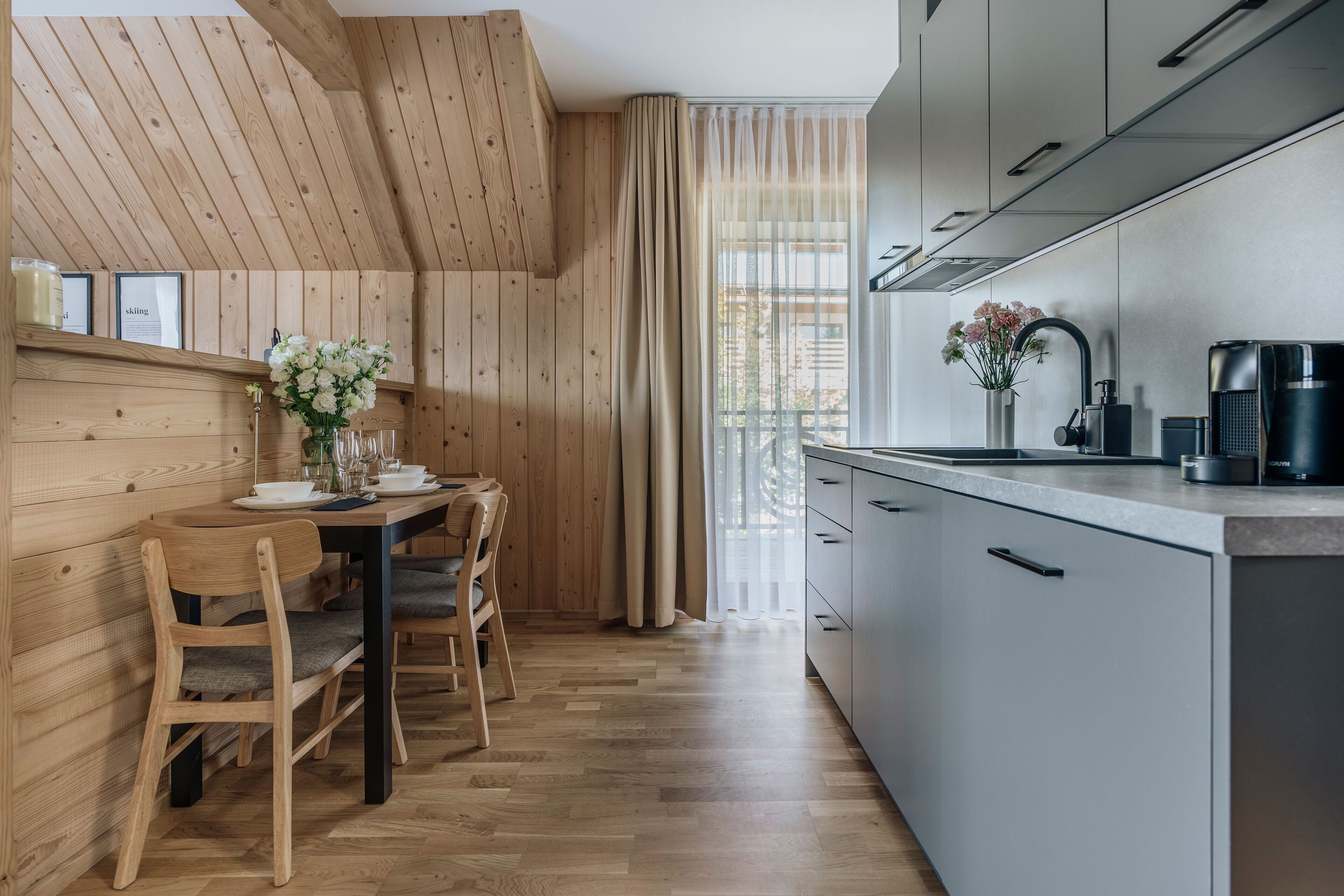 A modern kitchen with wooden walls, a dining area with a table and chairs, and a large window with curtains.