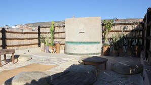 An outdoor patio with stone seating, a decorative planter, and a wall with a tree design. - namaste lodge experience (Tamraght)
